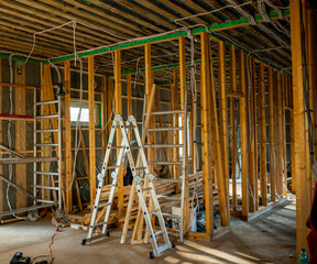 Under-construction home interior with wooden framing, electrical wiring, and ladder on site