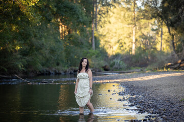 Woman holding up dress standing in tranquil creek