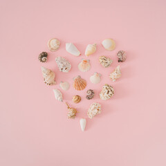 Creative summer layout with love heart symbol made with sea shells on light pastel pink background....