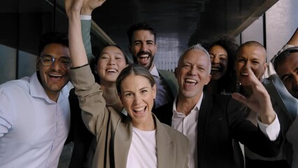 Diverse multiracial group of business people standing in office hallway looking cheerful at camera. Colleagues pose celebrating success by raising their hands at same time and smiling happy together