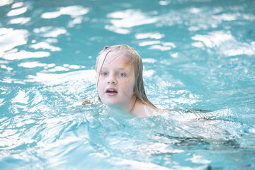 Fototapeta na wymiar Boy with long blonde hair swimming in resort swimming pool on vacation