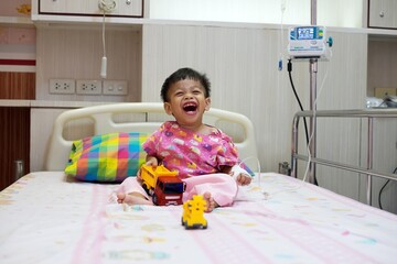 2-year-old baby in patient uniform Lying laughing, smiling in a hospital bed.
