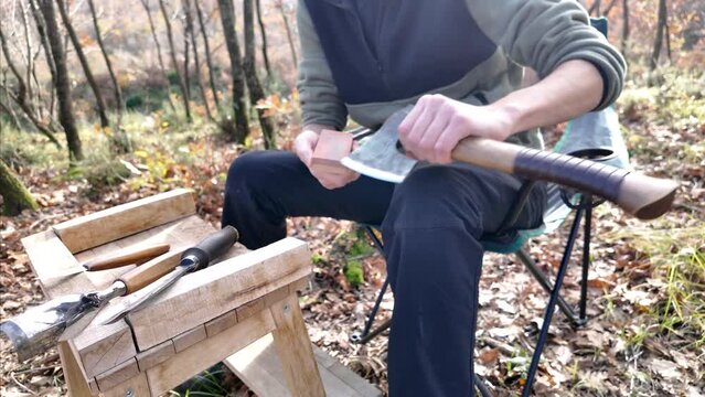 Close-up of sharpening an axe by using whetstone before wood carving. Carving equipments on the stand.