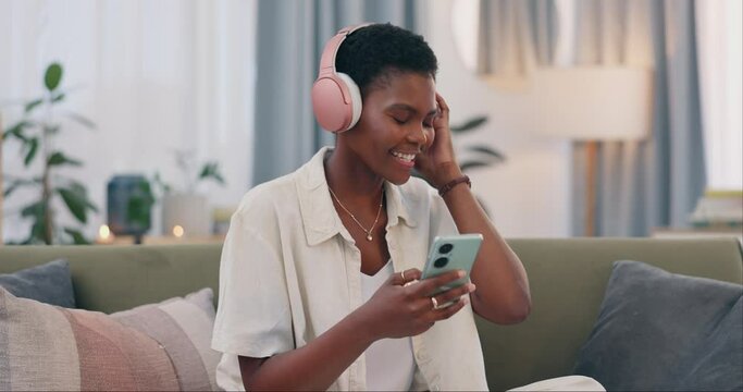 African woman, headphones and phone on sofa, relax and happy for streaming subscription in lounge. Girl, person and excited for audio tech, sound or reading with smile in living room on social media
