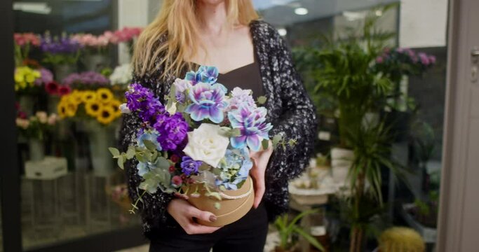 the girl shows a box of flowers with blue tulips, matiolas, white roses, chrysanthemum santini