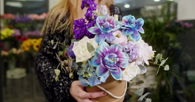 the girl shows a box of flowers with blue tulips, matiolas, white roses, chrysanthemum santini