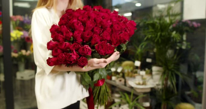 A girl in a flower store holds and shows a bouquet of medium-sized red roses 101 pieces