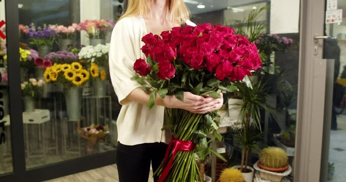 A girl in a flower store holds and shows a bouquet of medium-sized red roses 101 pieces
