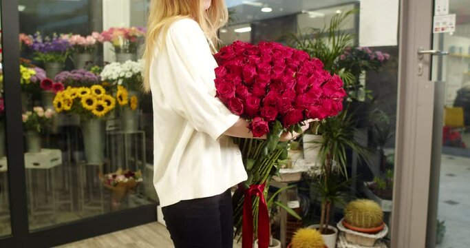 A girl in a flower store holds and shows a bouquet of medium-sized red roses 101 pieces