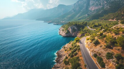  an aerial view of a road on the side of a mountain with a body of water in the foreground and a cliff on the other side of the road.