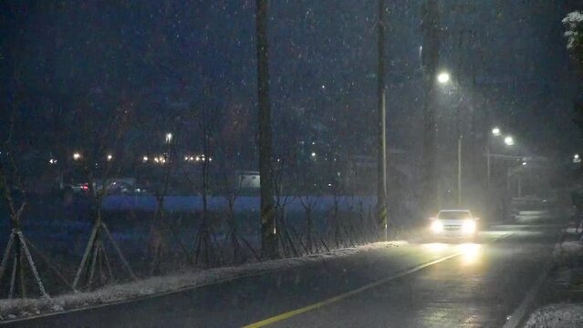 눈이 오는 시골 길에 자동차가 라이트를 키고 다가오는 한전한 한국의 겨울 도로 풍경