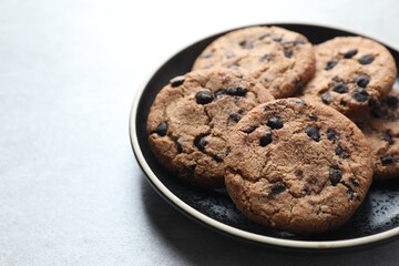 Plate with delicious chocolate chip cookies on light gray table, closeup. Space for text