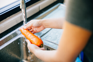 A young woman meticulously washes carrots in the kitchen sink emphasizing hygiene and organic food preparation. Illustrating the concept of washing vegetables before cooking. - Powered by Adobe