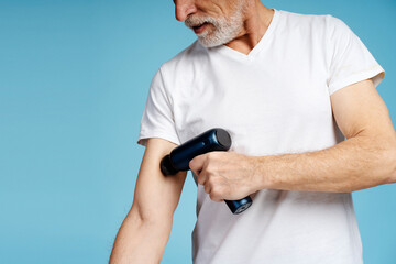 Naklejka premium Portrait of handsome senior man, pensioner wearing white t shirt using massager gun, recovery