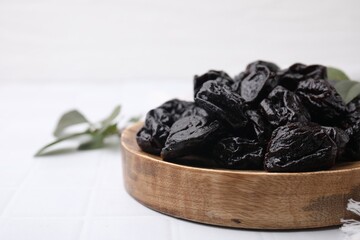 Sweet dried prunes on white tiled table, closeup. Space for text