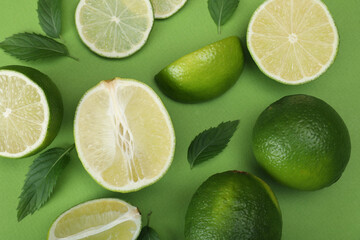 Flat lay composition with fresh limes and leaves on green background