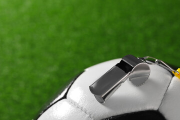 Football referee equipment. Soccer ball and metal whistle on green grass, closeup with space for...