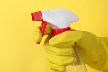 Woman holding plastic spray bottle on yellow background, closeup