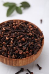 Aromatic cloves in bowl on white tiled table, closeup