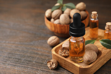 Nutmeg essential oil and nuts on wooden table, closeup. Space for text