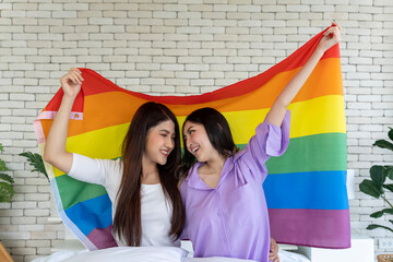 LGBTQ+ Pride: Two Smiling Young Women Hold Rainbow Flag on Bed