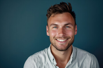 A man with a beard is smiling in front of a blue background
