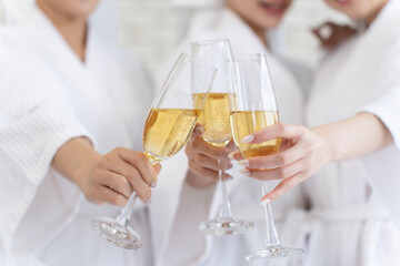 close-up of three young women wearing white bathrobes and wet hair wrapped in fluffy white towels hold wine glasses outstretched