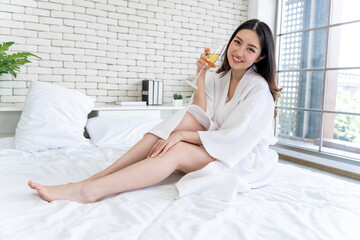 Asian woman in bathrobe holding wine on bed, lifestyle portrait of female relaxing