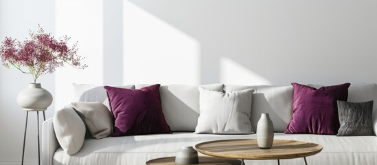 Lilac and burgundy pillows on grey settee in bright living room, with heather on coffee table and empty white wall with copy space.