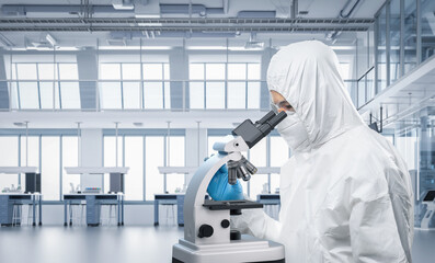 Worker or scientist wears white coverall suit look through microscope in laboratory