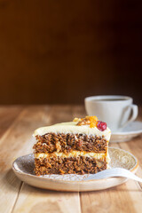 A slice of carrot cake with cream cheese frosting on a plate with a mug of coffee in the background