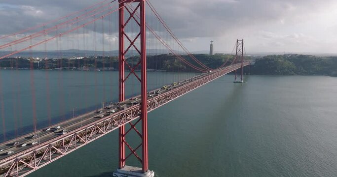 Aerial drone shot towards the 25th April Bridge, Ponte 25 de Abril, and Cristo Rei in Lisbon, Portugal, Europe. Afternoon with clouds. Shot in 5K ProRes 422 HQ