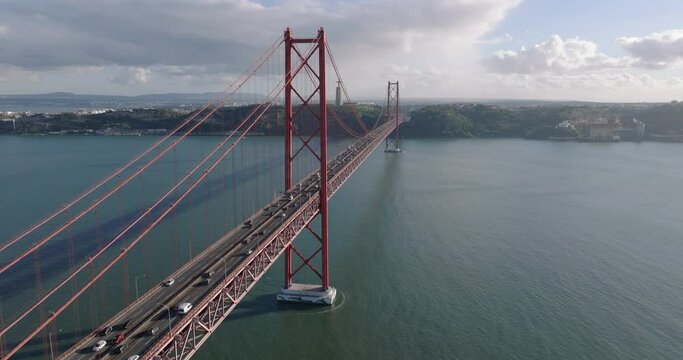 Aerial drone shot towards the 25th April Bridge, Ponte 25 de Abril, and Cristo Rei in Lisbon, Portugal, Europe. Afternoon with clouds. Drone orbiting. Shot in 5K ProRes 422 HQ