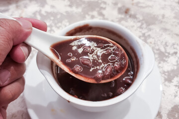 Hand with spoon scooing a spoonful of red bean soup, popular desert among Asian Chinese