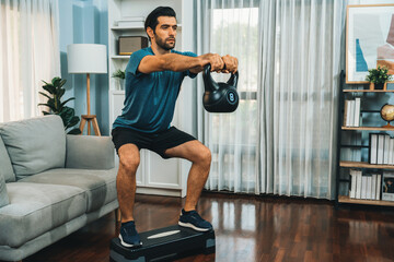 Athletic body and active sporty man doing squat with kettlebell weight for effective targeting muscle gain at gaiety home as concept of healthy fit body home workout lifestyle. - obrazy, fototapety, plakaty