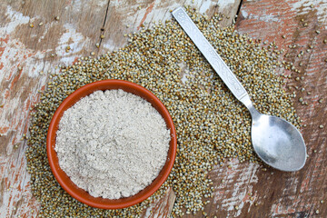 Pearl millet powder in a bowl with seeds on wooden background 