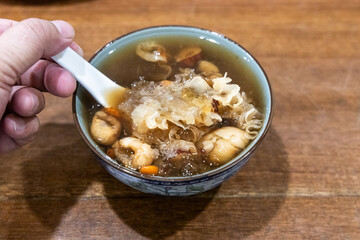Hand with spoon scooping longan with snow fungus goji seaweed soup, popular desert among the Chinese