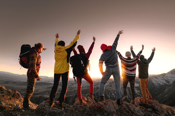 Big group of happy tourists or hikers are standing at mountain top and enjoys sunset. Active lifestyle concept