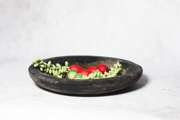 Green and red palm fruits (buah palem) on wooden plate.
