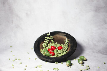 Green and red palm fruits (buah palem) on wooden plate.