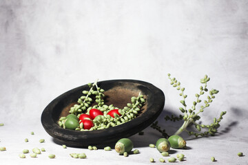 Green and red palm fruits (buah palem) on wooden plate.