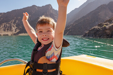 happy smiling little boy enjoying sailing on a mountain lake on a catamaran. Summer travel and...