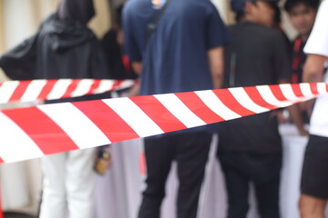Selective focus on barricade or tape barrier in red and white with unfocused background of queuing...
