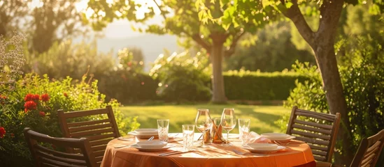 Fotobehang Orange tablecloth covering wooden dining table on green garden terrace. © 2rogan