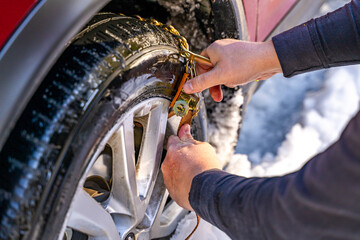 Man's hands putting on snow chains on the car wheel