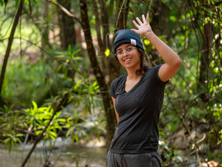 Femme souriante et sympathique qui dit bonjour la main levée de façon amicale dans la forêt © Romane