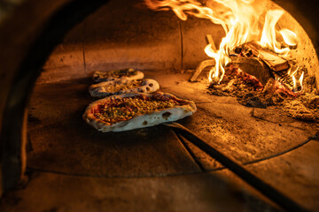 Traditional oven for baking pizza with burning wood and shovel. The cook rotates the pizza in the...