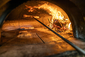 Traditional oven for baking pizza with burning wood and shovel. Neapolitan pizza is finished on a...