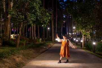 Asian child camper or young kid girl travel camping and standing holding warm white lantern or lamp alone at twilight night in nature tree garden resort on holiday vacation at Doi Bo Luang Forest Park