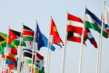 Group of flags of many different nations against blue sky